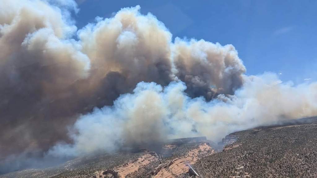 Helikopter pemadam kebakaran terbang di atas area hutan yang terbakar dengan kepulan asap tebal membubung tinggi di pegunungan barat Colorado.