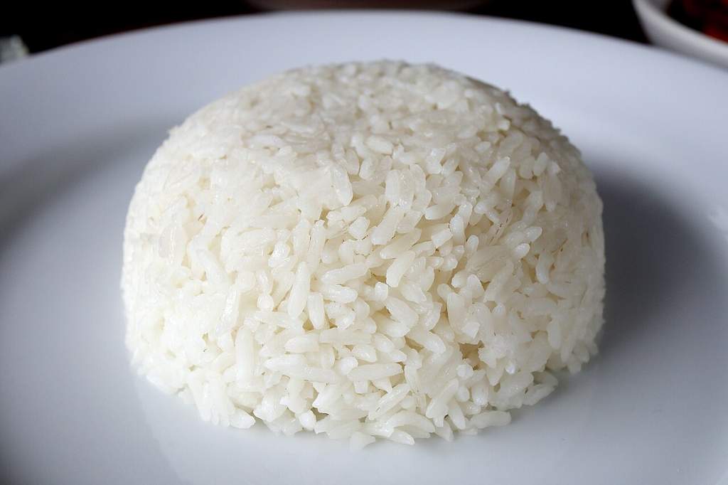 Semangkuk nasi putih hangat yang pulen disajikan di atas meja kayu dengan latar belakang dapur tradisional.